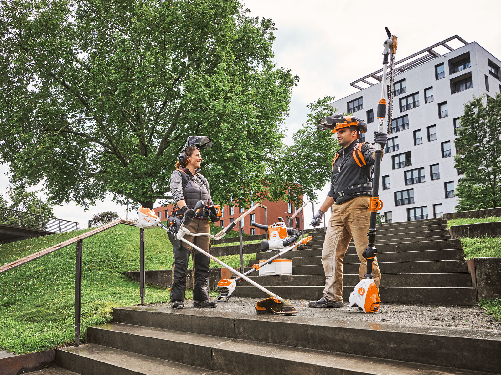 Grupa osób pracuje narzędziami ogrodniczymi STIHL w zielonej przestrzeni. Są wyposażeni w nożyce do cięcia i sprzęt ochronny.
