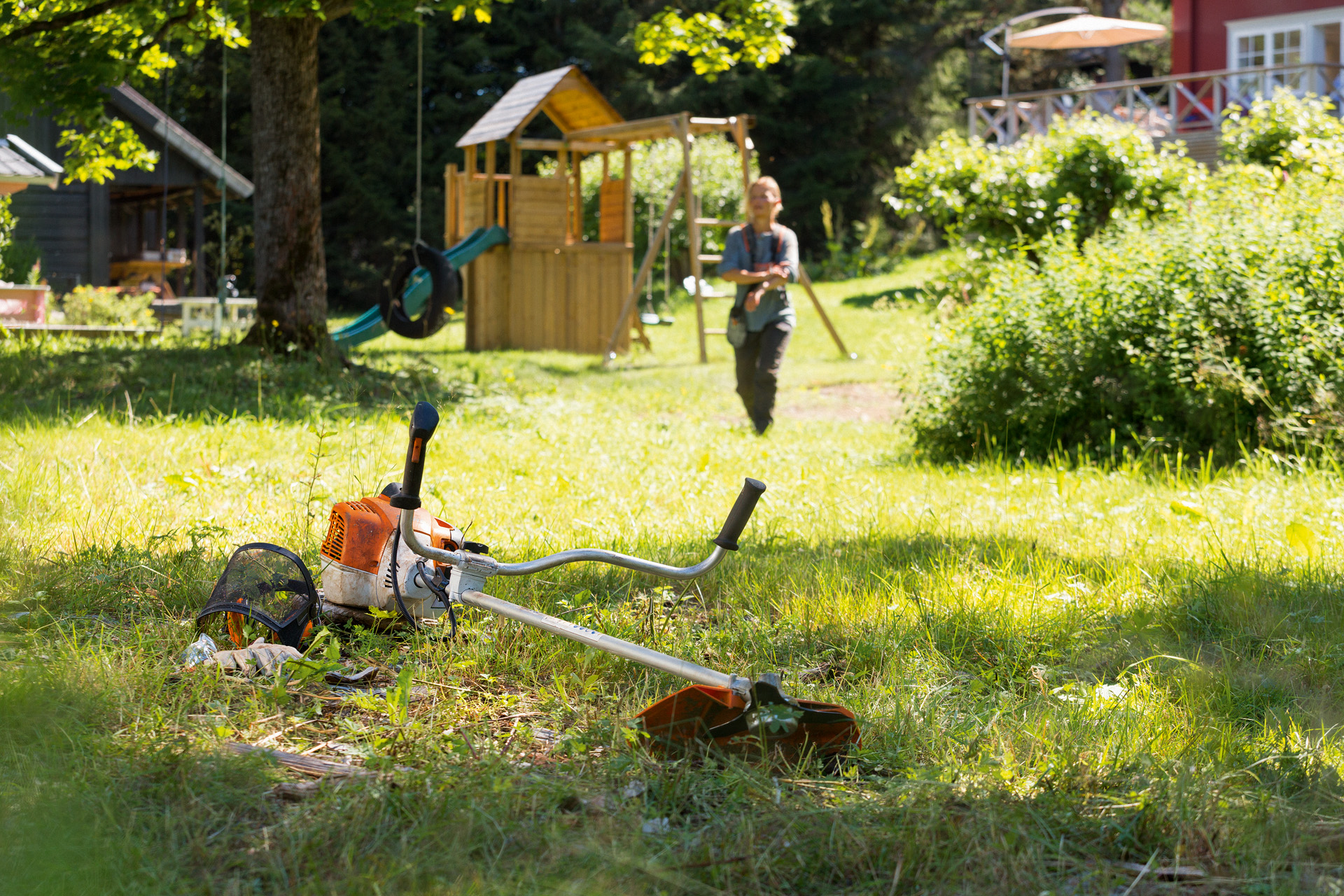 Kosa mechaniczna STIHL FS 240 leży w trawie, w tle kobieta przygotowuje się do konserwacji 