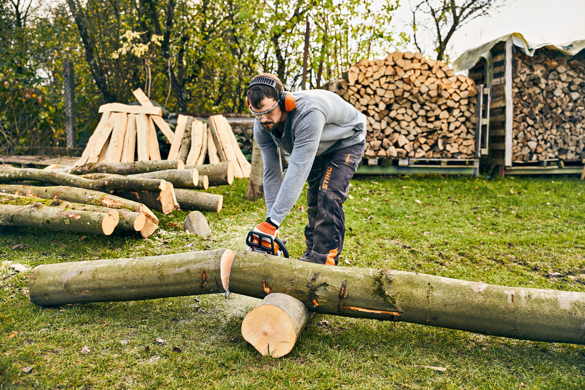 Mężczyzna w okularach ochronnych i ochronnikach słuchu piłuje kłodę piłą spalinową STIHL MS 180