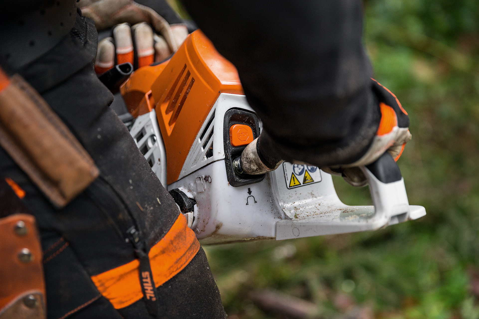 Osoba w odzieży ochronnej uruchamia benzynową pilarkę łańcuchową STIHL MS 500i na ziemi w lesie liściastym