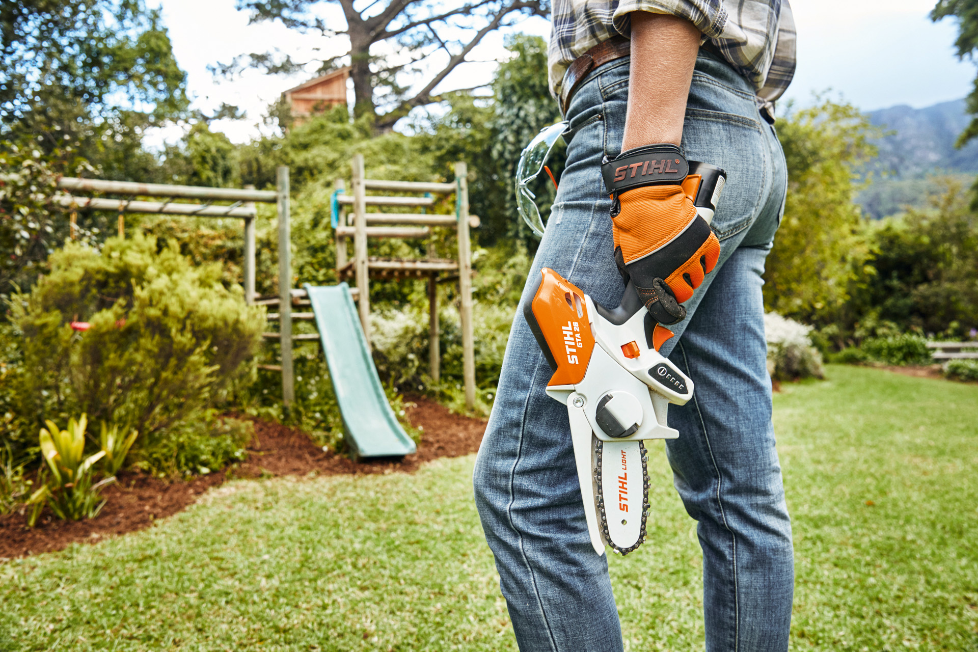 Osoba z akumulatorową przecinarką do drewna STIHL GTA26 stoi w ogrodzie przed zsuwnią