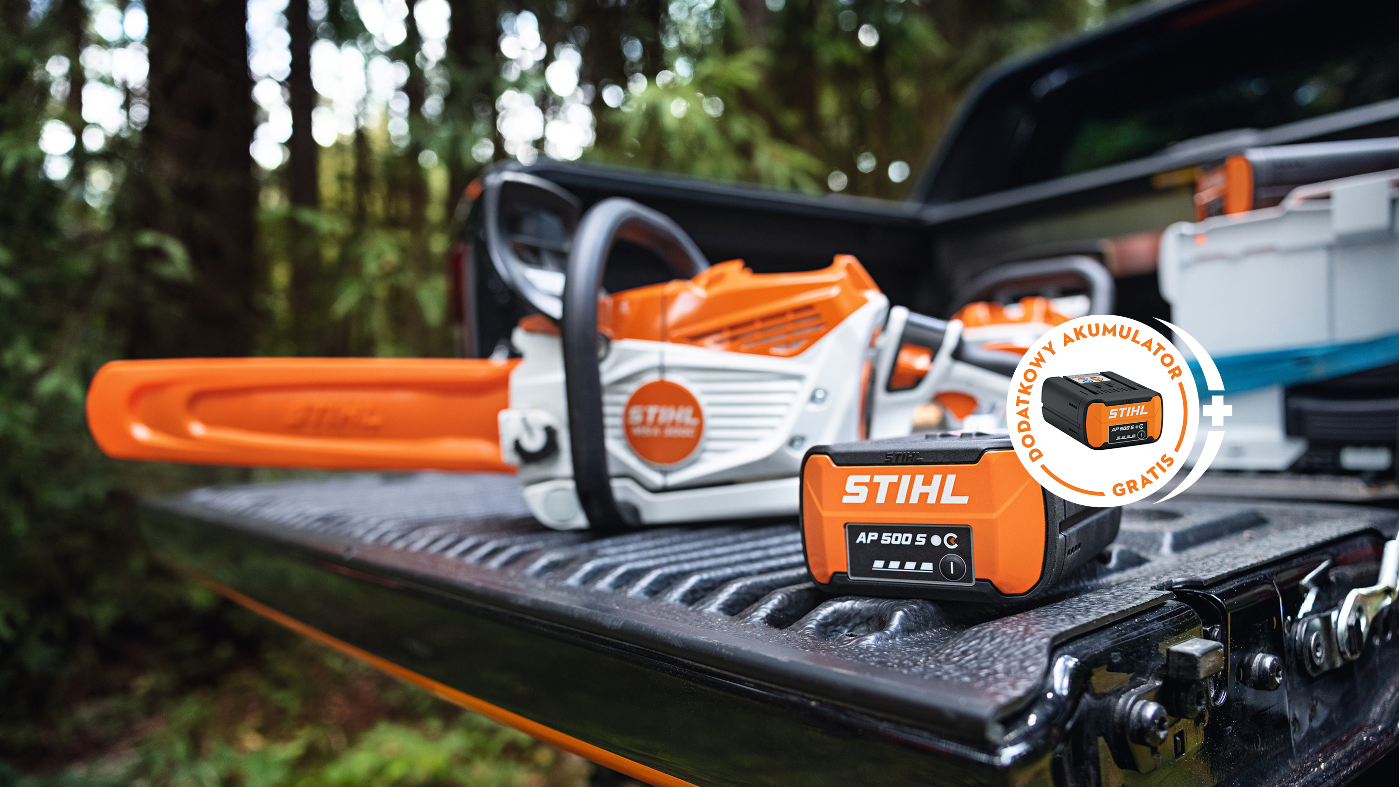 Akumulator STIHL AP 500 S na powierzchni ładunkowej pick-upa wraz z nową akumulatorową piłą łańcuchową STIHL MSA 300 oraz tabliczka z akumulatorem STIHL i napisem „Odbierz akumulator gratis”.