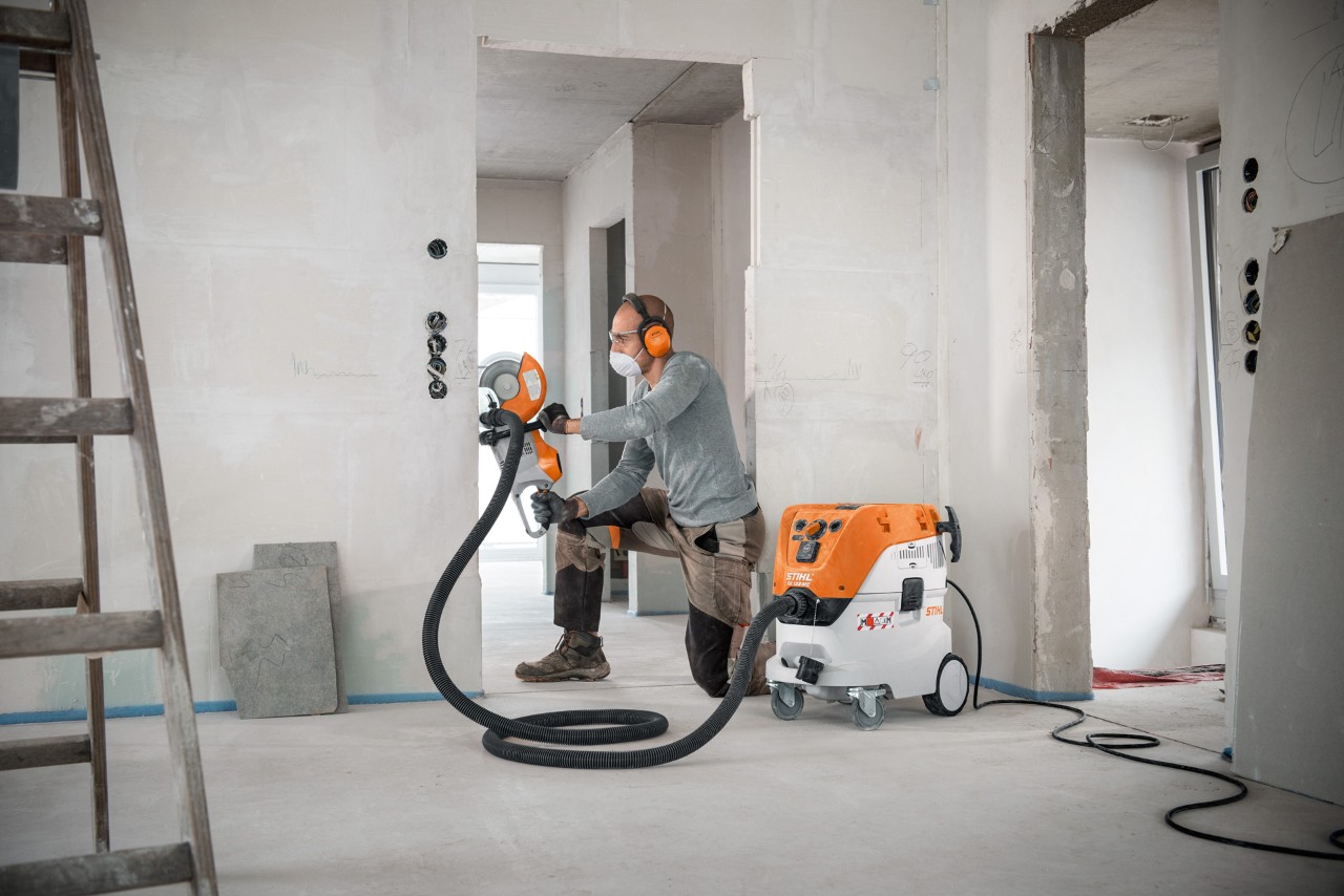 Mężczyzna używa odkurzacza STIHL do czyszczenia na mokro i sucho SE 133 ME podczas pracy ze szlifierką tarczową STIHL TSA 230