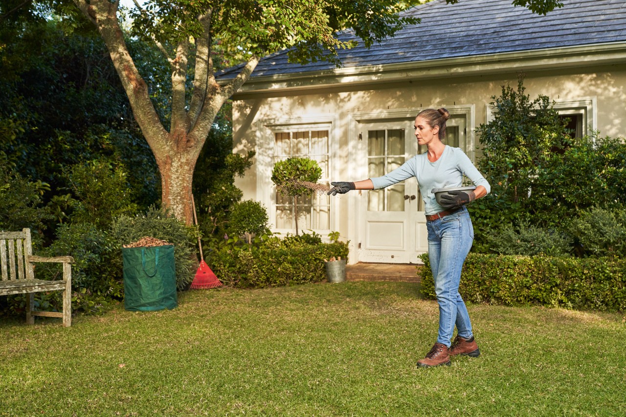 A woman wearing work gloves spreading lawn lime on a lawn.